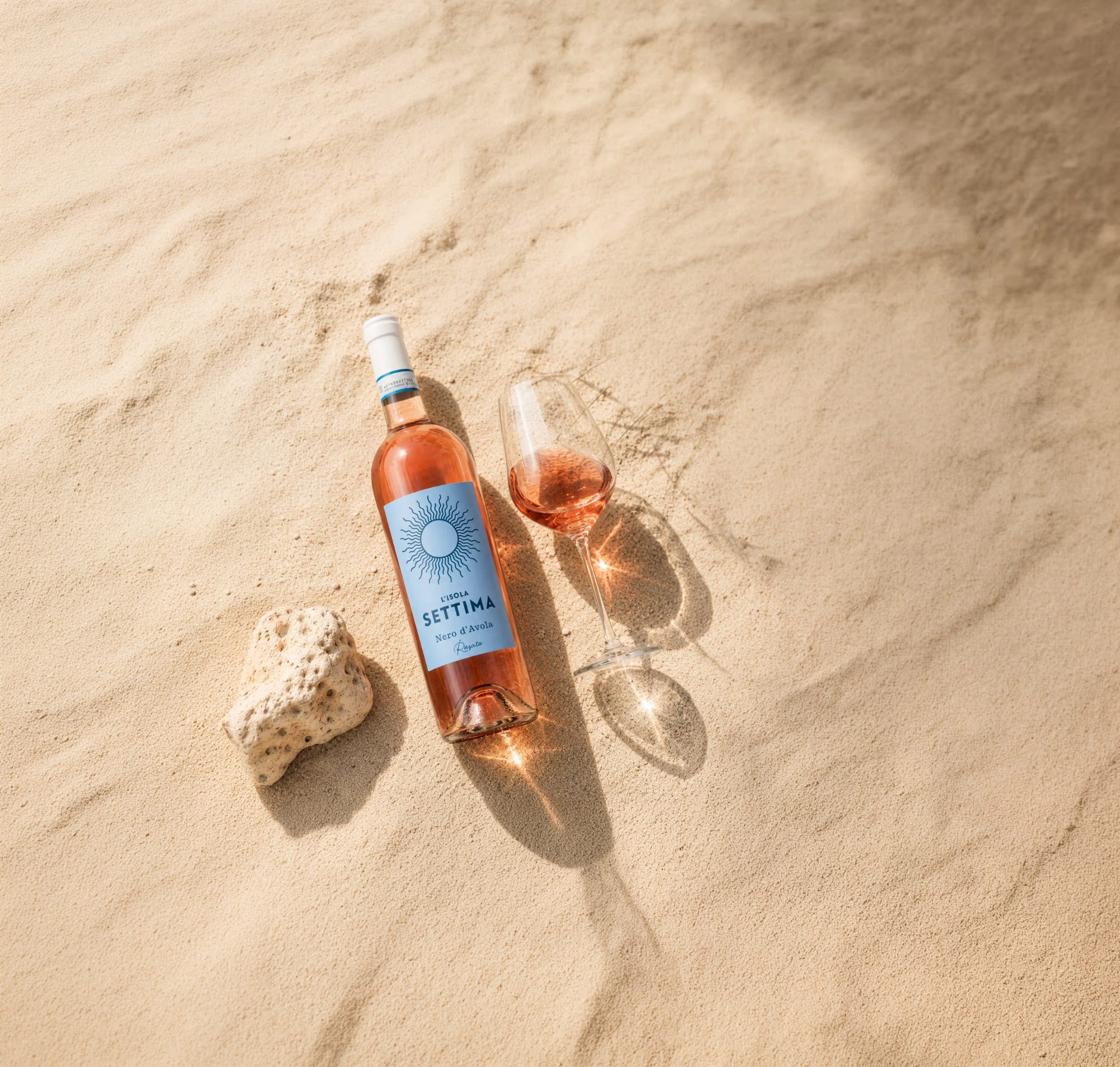 Weinetikett »L'Isola Settima« für Alibrianza – Rosato-Flasche und Glas am Strand in der Sonne